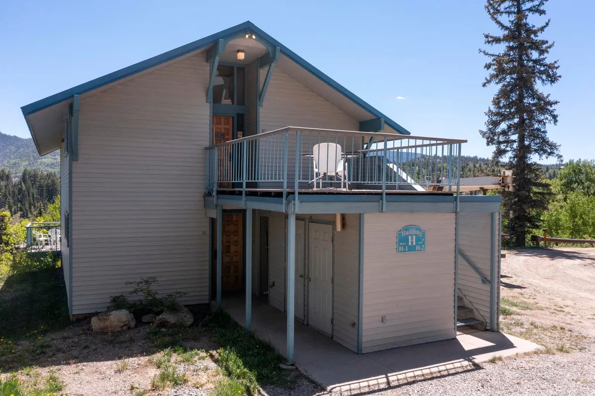This exterior image highlights the balcony space with outdoor seating, the entrance, and lush greenery around. The balcony area is showcased as an inviting spot to relax and enjoy the crisp mountain air or watch snowfall—blurring the lines between indoor comfort and outdoor beauty.