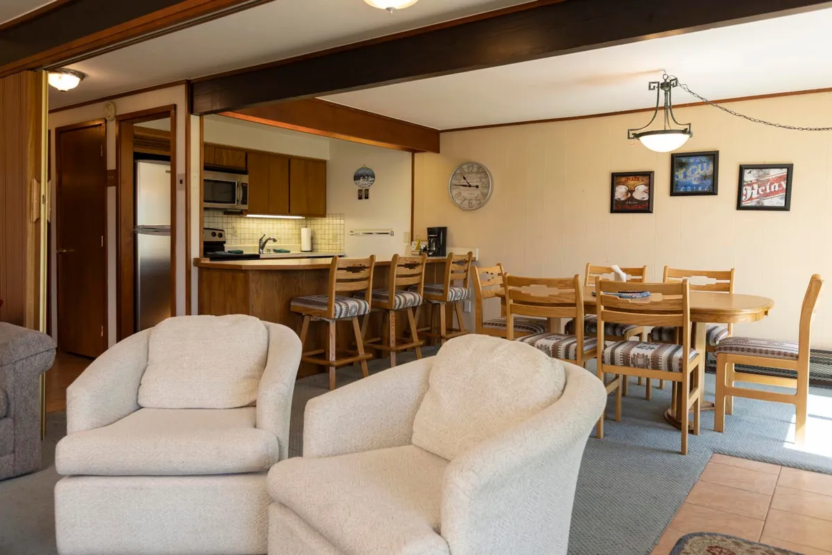 This image features a cozy interior that includes comfortable armchairs, a dining table, and a visible kitchen area. The setup suggests a welcoming space for family meals or casual gatherings, with the kitchen and dining area seamlessly integrated for ease and convenience.