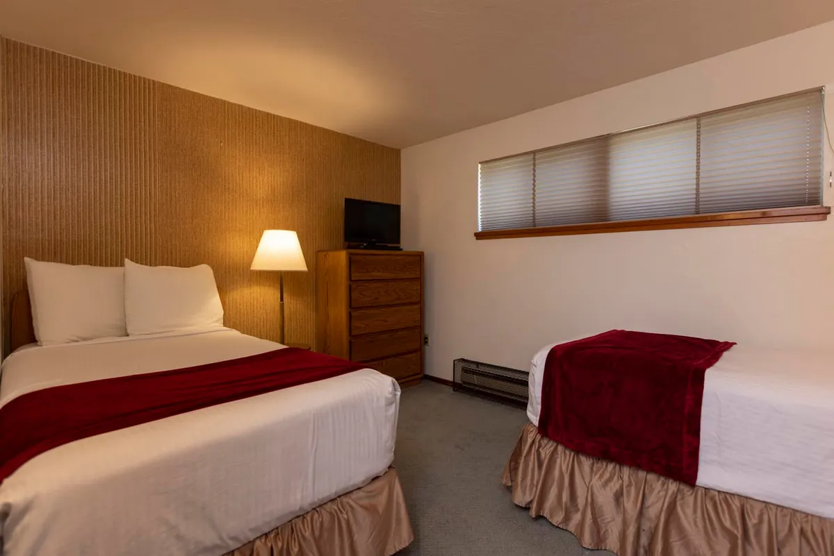 A bright and inviting second bedroom featuring twin beds with crisp white linens and bold red accents, a wooden dresser, table lamp, and a TV for entertainment. The layout encourages shared moments and is ideal for children or friends traveling together.