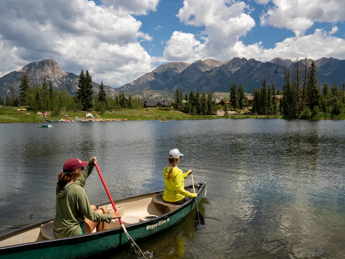 A serene mountain lake with a canoe on the water, surrounded by towering peaks and participants enjoying outdoor activities. The scene is set at sunset, emphasizing the beauty and adventure of the local landscape beyond the property.